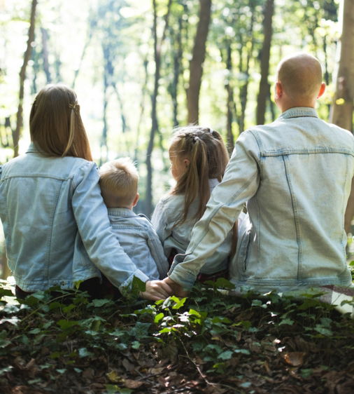 man and woman holding hands together with boy and girl looking at green trees during day