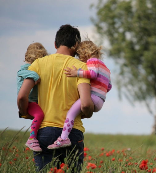 man carrying to girls on field of red petaled flower
